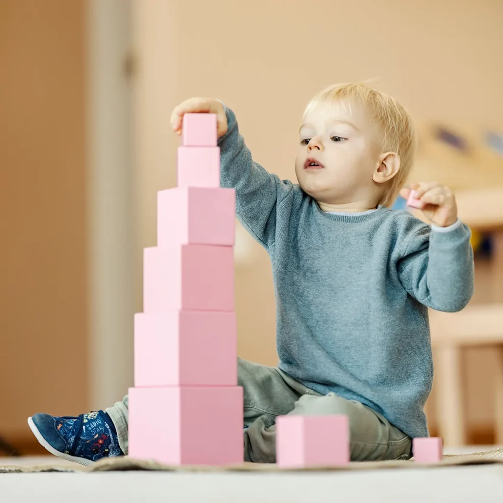 Child stacking pink montessori blocks at child care