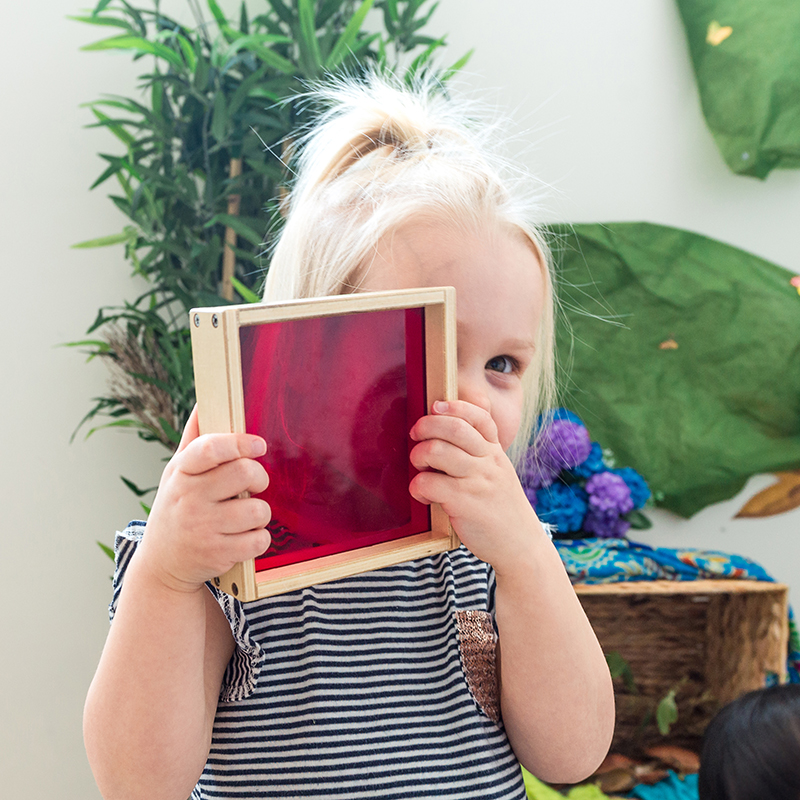 Child looking through square red sensory toy