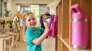 A young girl who is preparing for school is placing a bag into a school shelf