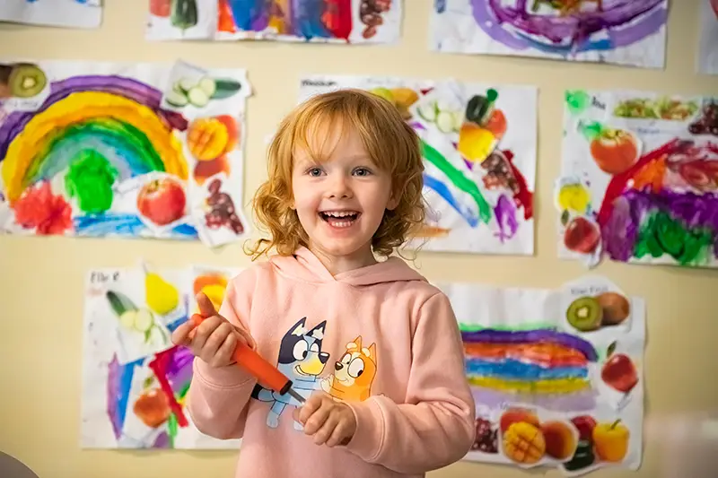 Kindergarten girl smiling in front of artwork