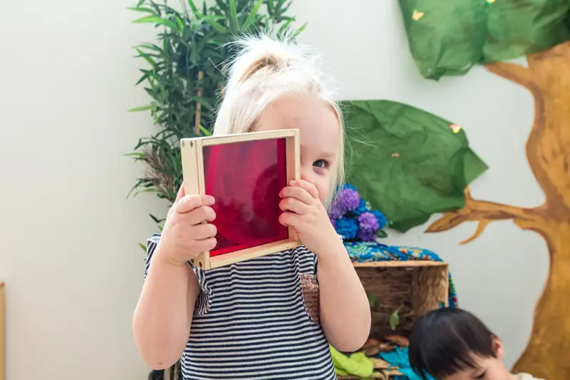 toddler girl looking through red sensory toy