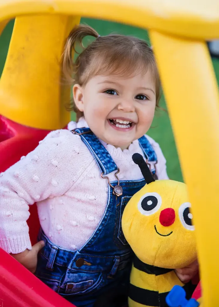 toddler in Little Tikes coupe car holding bee soft toy