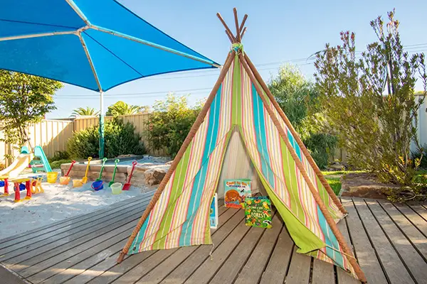 Blue and green fabric covered tepee with a sandpit in background