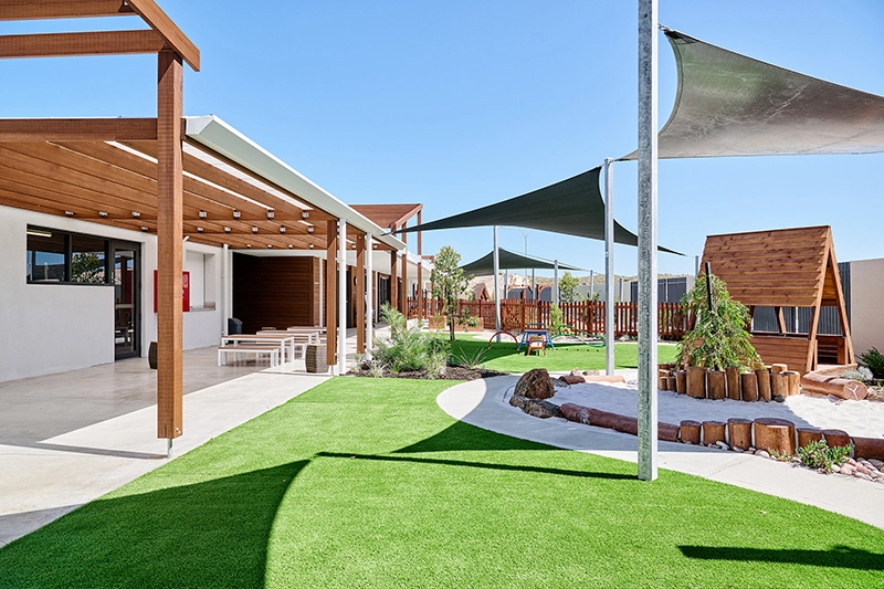 Outdoor playground at Amberton Beach child care with plenty of grassy areas, shade sails, sandpit and wooden tepee.