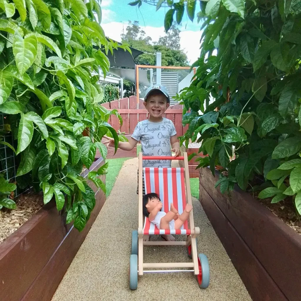 Preschool boy pushing doll in pram through vin archway at Everton Hills preschool