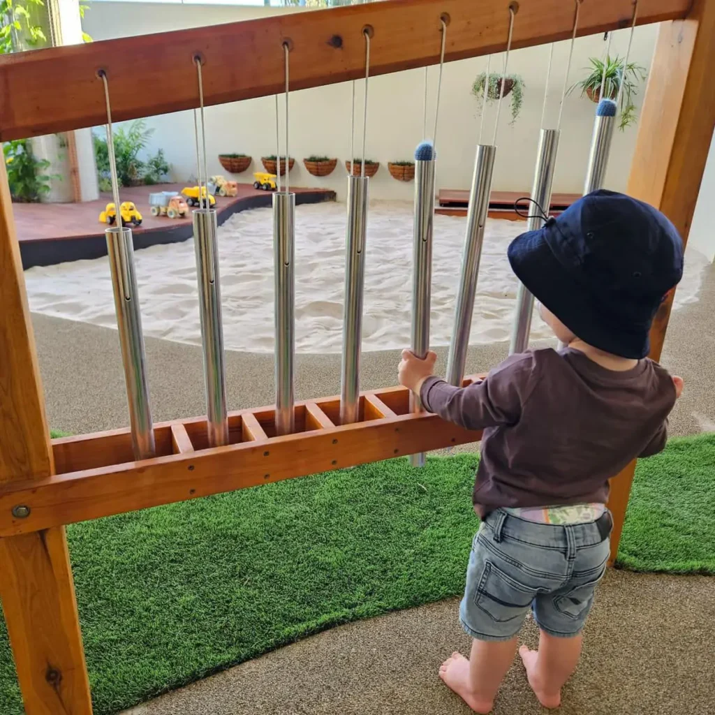 Child playing musical chimes in outdoor playground at Everton Hills day care