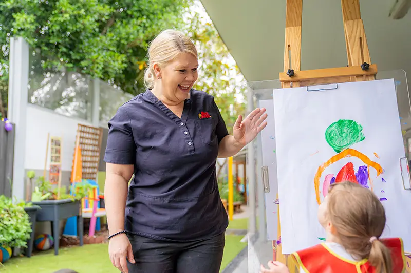 Early childhood educator saying hello to child painting