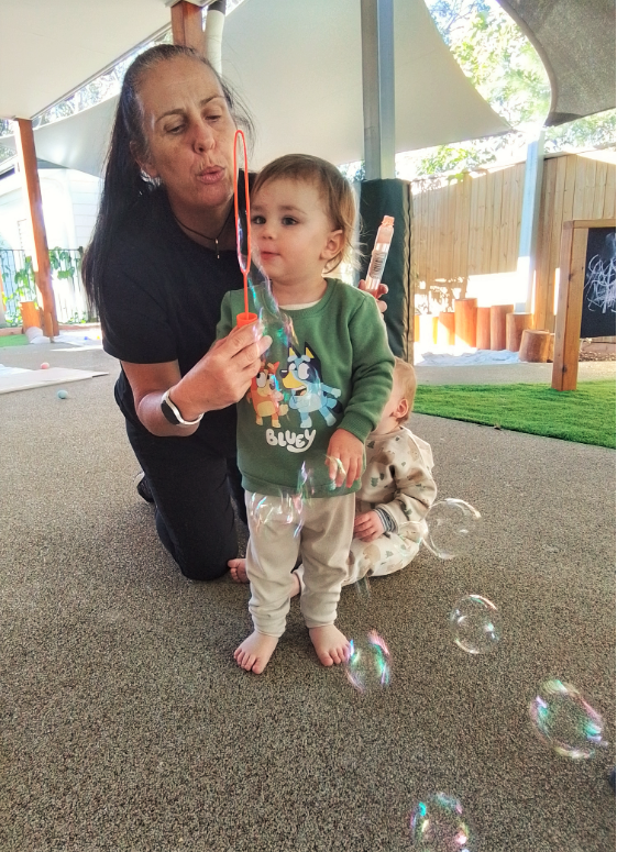 Early childhood educator blowing bubbles for child