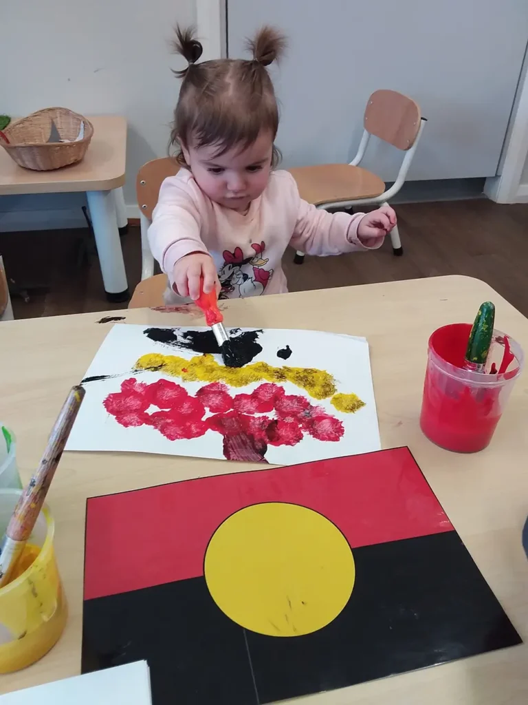 Child painting Aboriginal flag at Busy Bees at Cameron Park