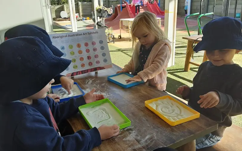 Children drawing Aboriginal symbols in sand