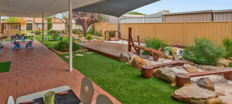 Outdoor nature play area with balance elements and landscaped gardens.
