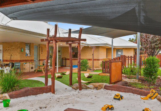 Outdoor learning area with activity table, play equipment and shaded play space.