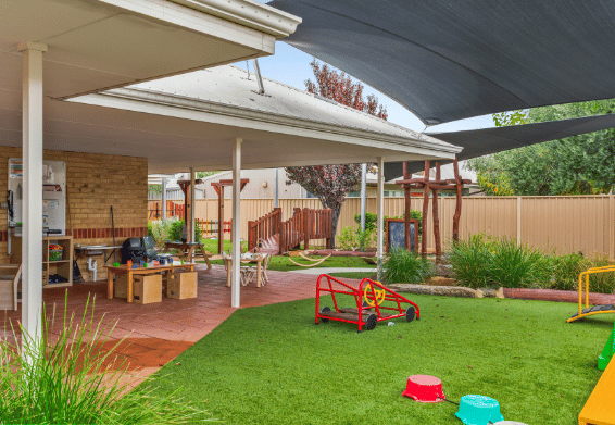Outdoor play area with shade sails, decking and open grassed spaces.