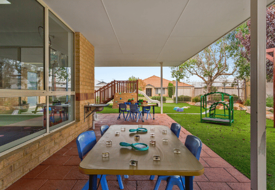 Outdoor learning space with children's tables, play equipment and shaded grassed areas.