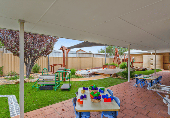 Outdoor play area with activity tables, climbing equipment and shaded play spaces.