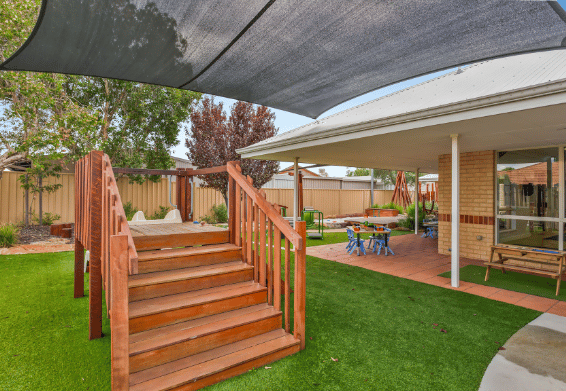 Outdoor play area with timber steps, shade sails and open grassy spaces.