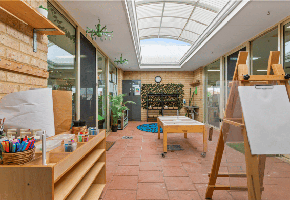 Covered outdoor learning area with activity tables, shelving and natural light.