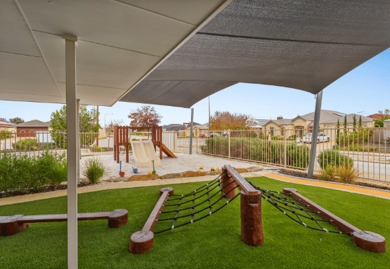 Nature-inspired outdoor learning environment with climbing equipment, sand play, decking, garden features and shaded areas for exploration and play-based learning.
