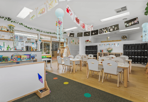 Classroom learning environment with child-sized tables and educational displays.