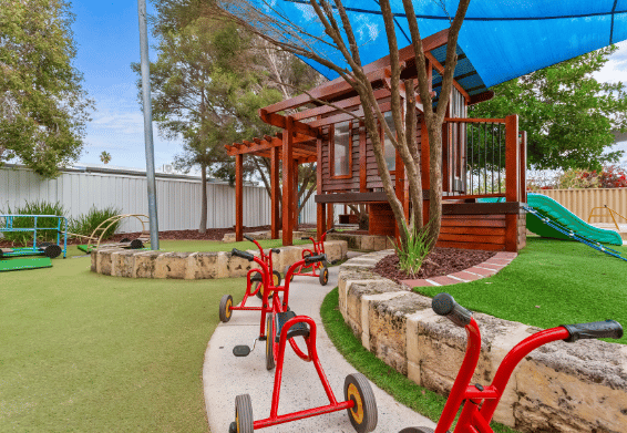 Outdoor play area with timber cubby structure and tricycles.