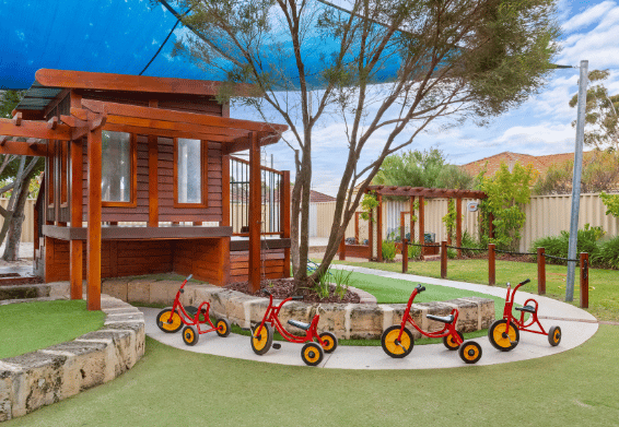 Timber play structure surrounded by trees and children's tricycles.