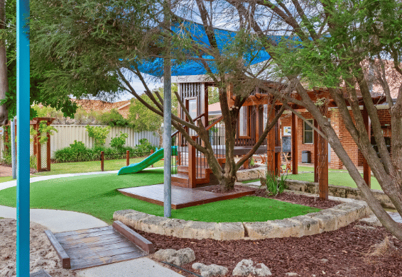 Outdoor playground with timber cubby house and natural landscaping.