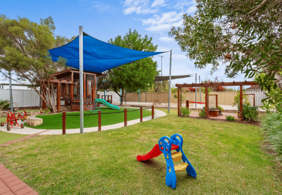 Outdoor play area with shade sails, grassed spaces and play equipment.