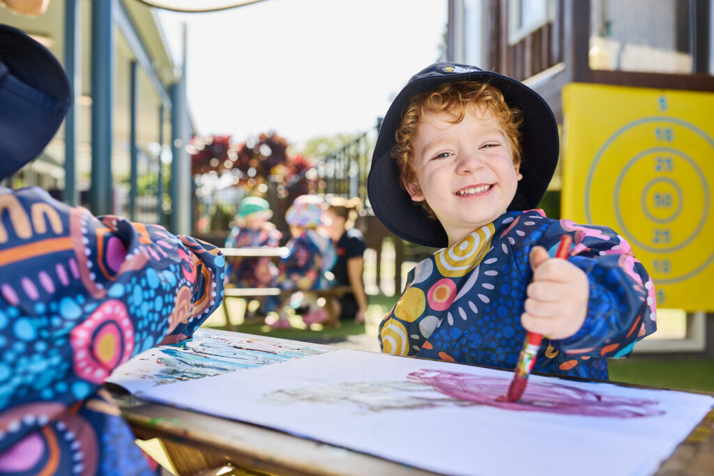 Child smiling while participating in a creative learning activity.