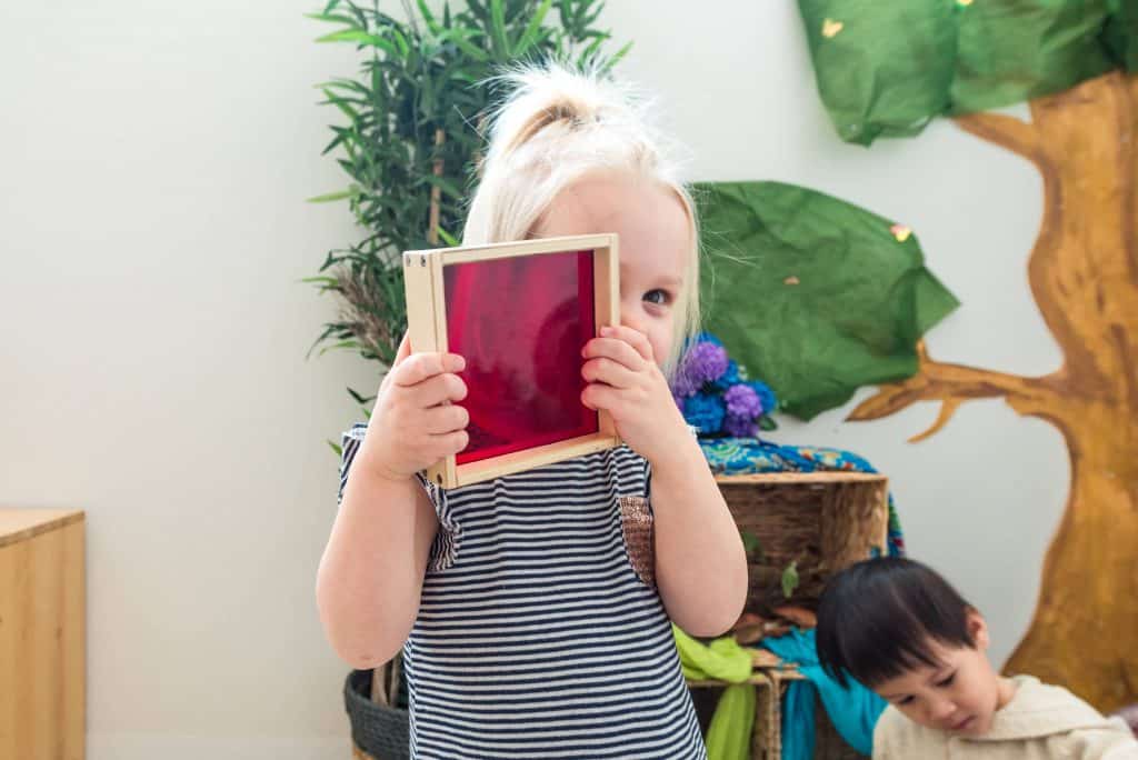 Young preschool girl looking through red transparent toy