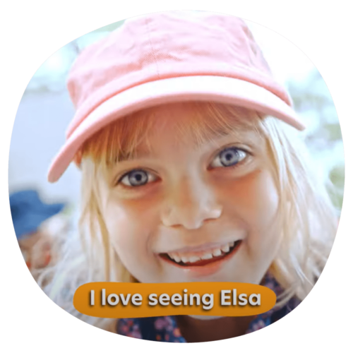 A young girl wearing a pink cap smiles with the text "I love seeing Elsa" displayed at the bottom of the image, capturing a delightful moment in early learning.