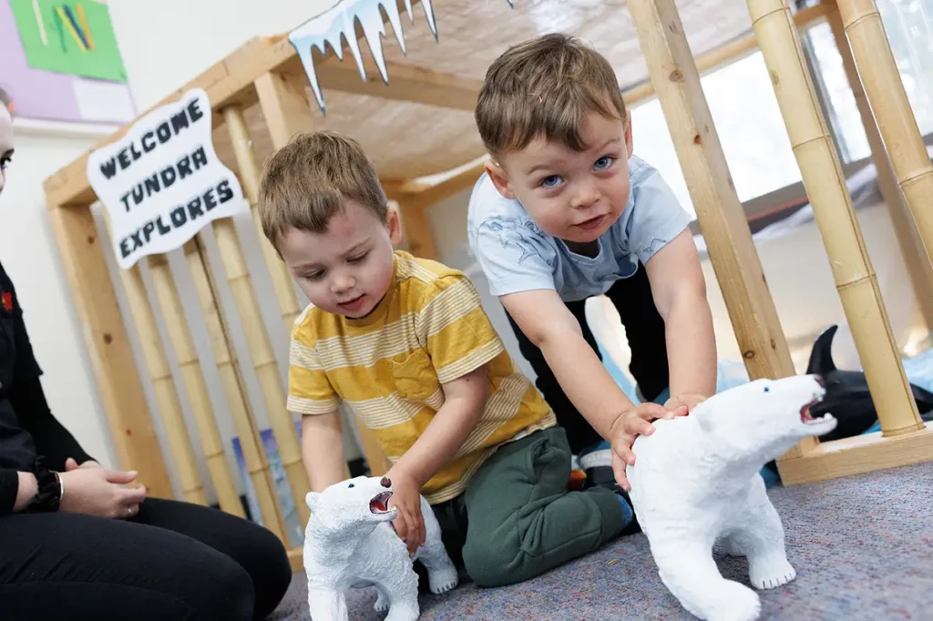 Two young children play with toy polar bears next to a wooden structure; a sign behind them reads "WELCOME TUNDRA EXPLORERS.