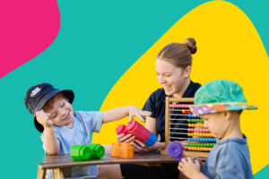 A Busy Bees Educator smiling as two young children play with colourful blocks and an abacus at a low table.