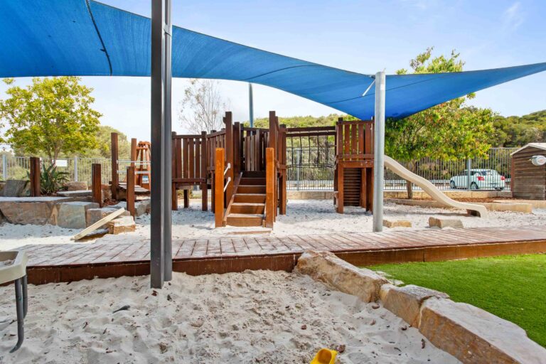 Playground at Busy Bees Aveley with a timber climbing fort, slide and sandpit under a shade sail