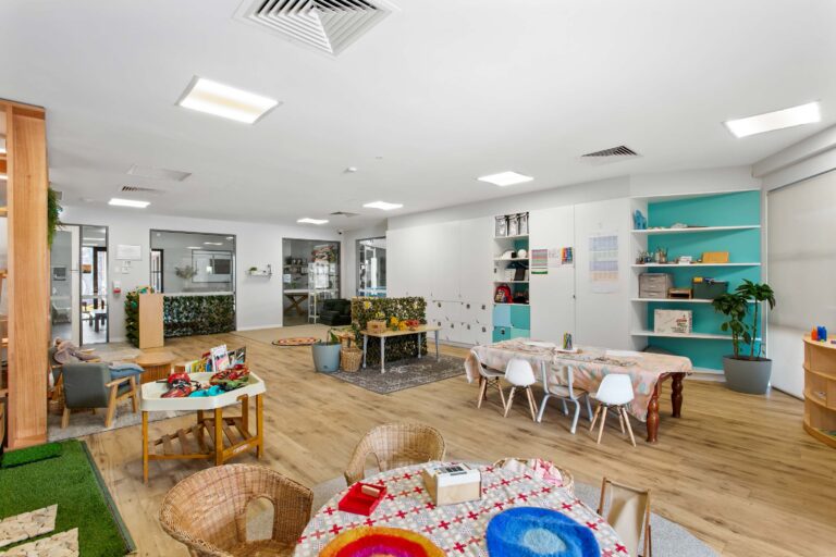 Preschool room at Busy Bees Aveley with group tables, rattan seating and open shelving