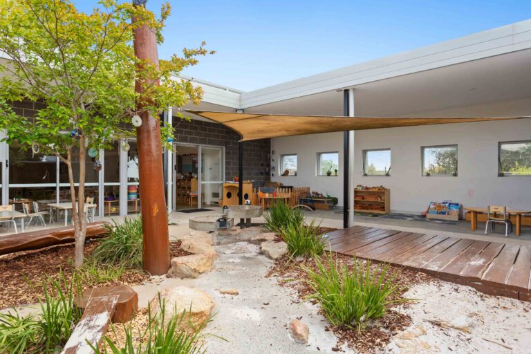 Outdoor courtyard at Busy Bees Banksia Grove Village with a shade sail, timber deck and native planting