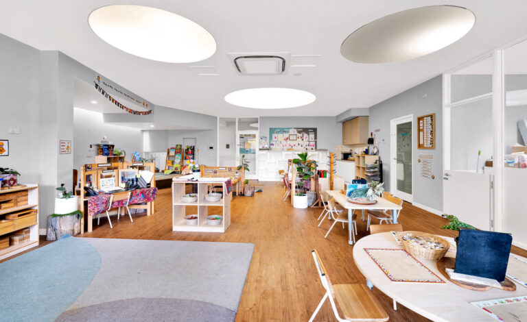 Activity room at Busy Bees Glenroy Station with display tables, a kitchenette and a round floor rug