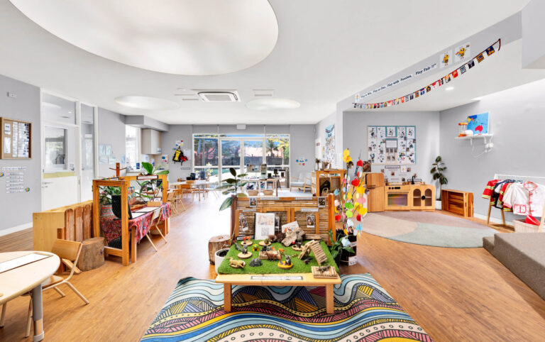 Preschool room at Busy Bees Glenroy Station with a patterned rug, home corner and nature small world table