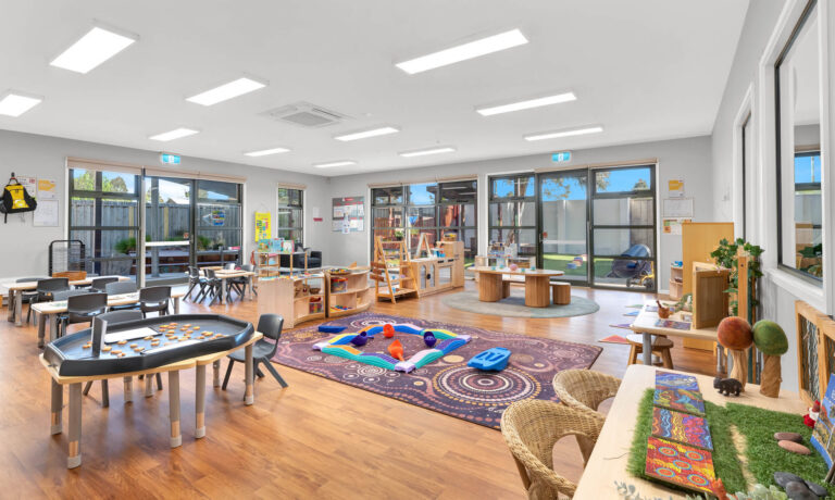 Open indoor learning space at Busy Bees Truganina with a patterned rug, loose parts play and a nature display table