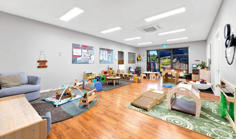 Nursery room at Busy Bees Truganina with soft play mats, a timber climbing ramp and a reading couch